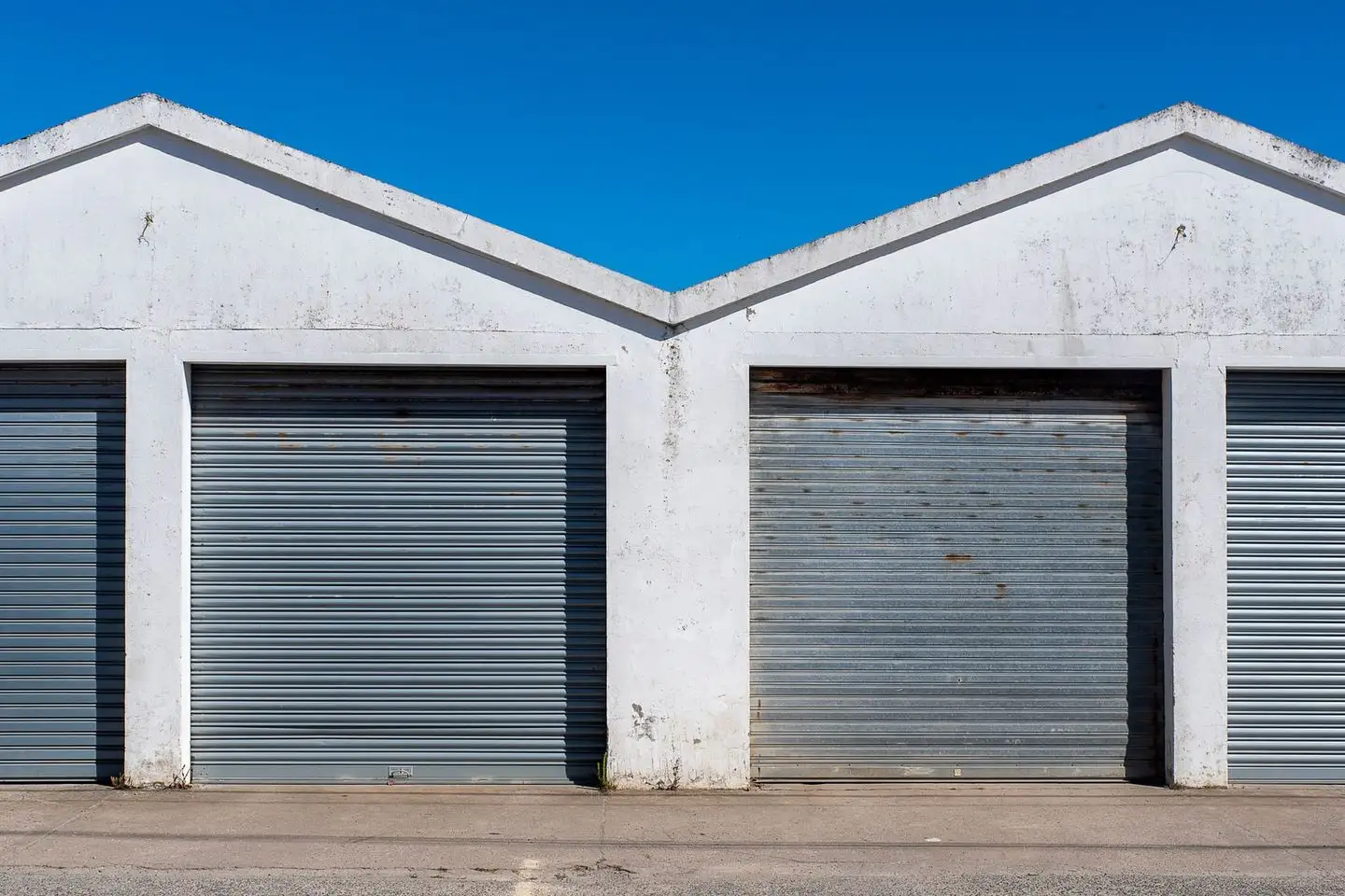 Row of roller-door sheds with a concrete apron under a clear blue sky